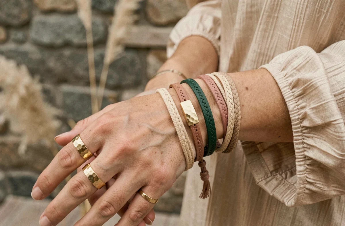 Gros plan sur des accessoires bohèmes empilés : bagues dorées martelées et bracelets en cuir et fil sur une main féminine